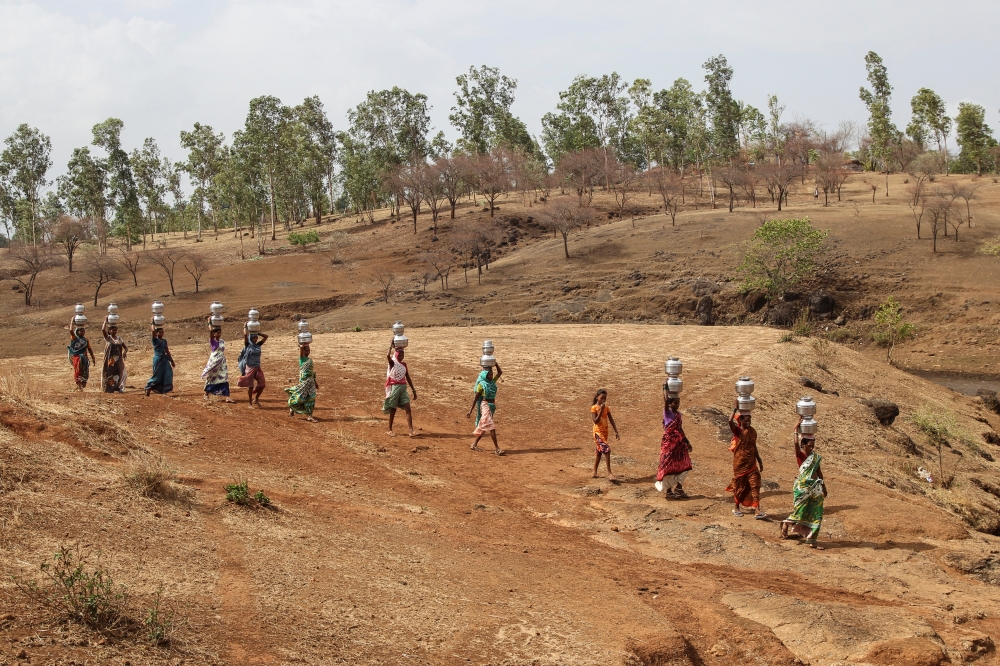 Women carry pitchers filled with water from an opening made to filter water next to a polluted lake in Thane, India June 13, 2019. REUTERS/Prashant Waydande