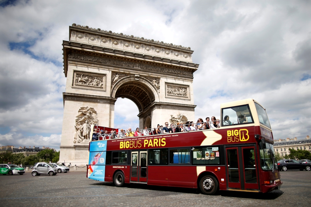 FILE PHOTO: Tourists ride in an open-air double-decker bus past the Arc de Triomphe in Paris, France, May 30, 2017. REUTERS/Charles Platiau/File Photo
 