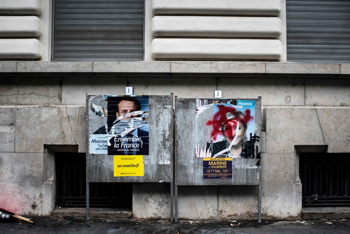 A picture shows vandalised campaign posters of Emmanuel Macron and Marine Le Pen in Lyon on May 1, 2017 ahead of  final round of the presidential election. AFP/Jeff Pach