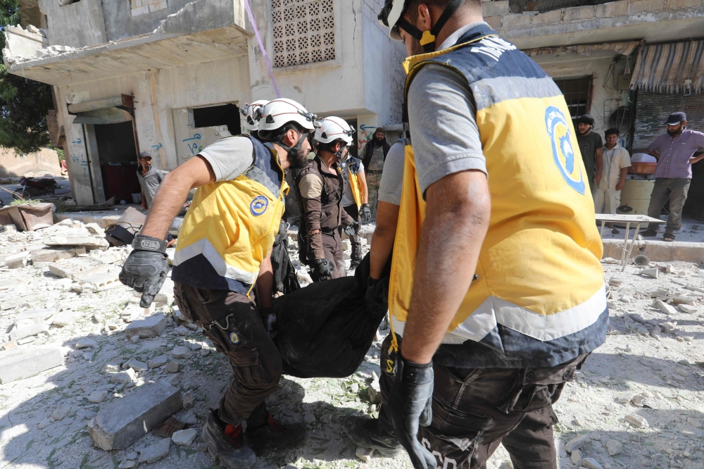 Members of the Syrian Civil Defence (White Helmets) carry away a body following a reported regime airstrike on the village of Kafriya, in Syria's Idlib province, on July 13, 2019. (AFP / Omar HAJ KADOUR)