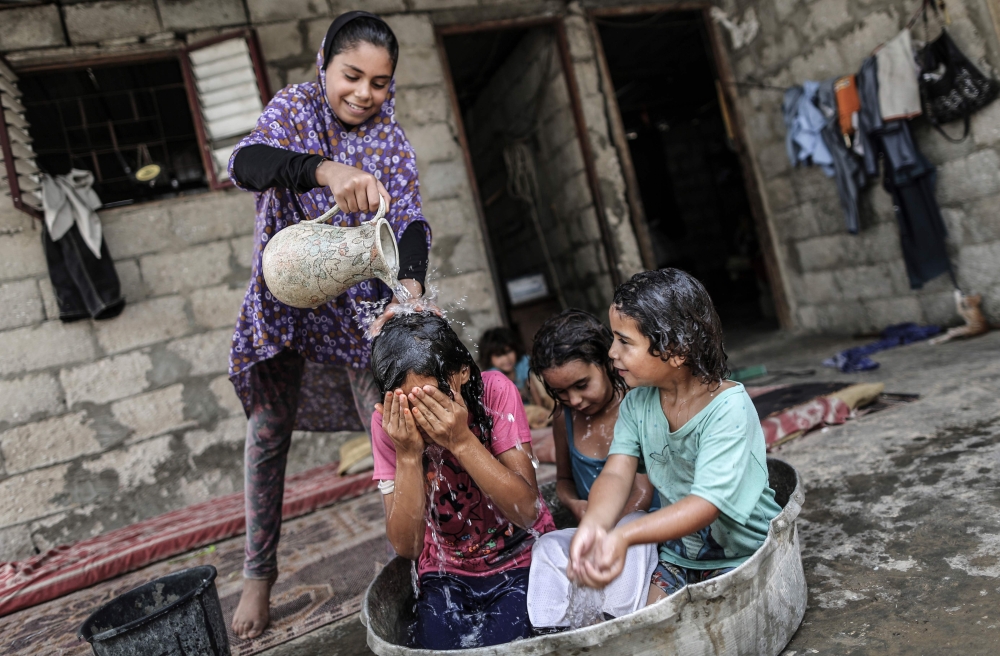 A Palestinian children take a bath in a slum on the outskirts of the Khan Yunis refugee camp, in the southern Gaza Strip on July 17, 2019, during a heat wave. AFP / Mahmud Hams
 