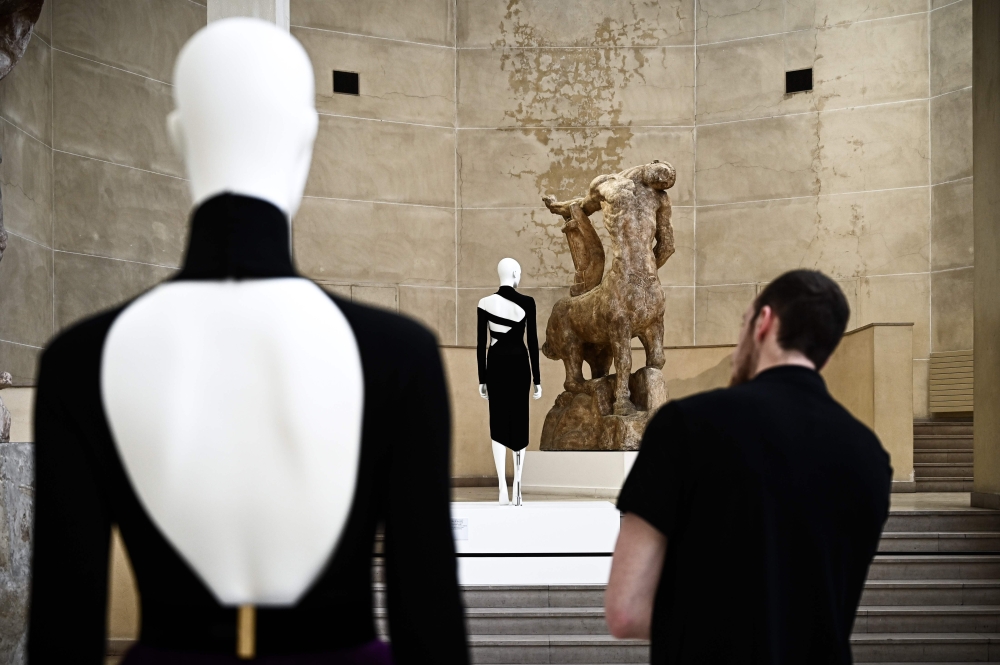 A man looks at a dress by Moroccan fashion designer Martine Sitbon (C) displayed next to a large plaster cast by French sculptor Antoine Bourdelle (1861-1929) at the off-site exhibition 'Back Side / Fashion from Behind' by the Palais Galliera held at the 
