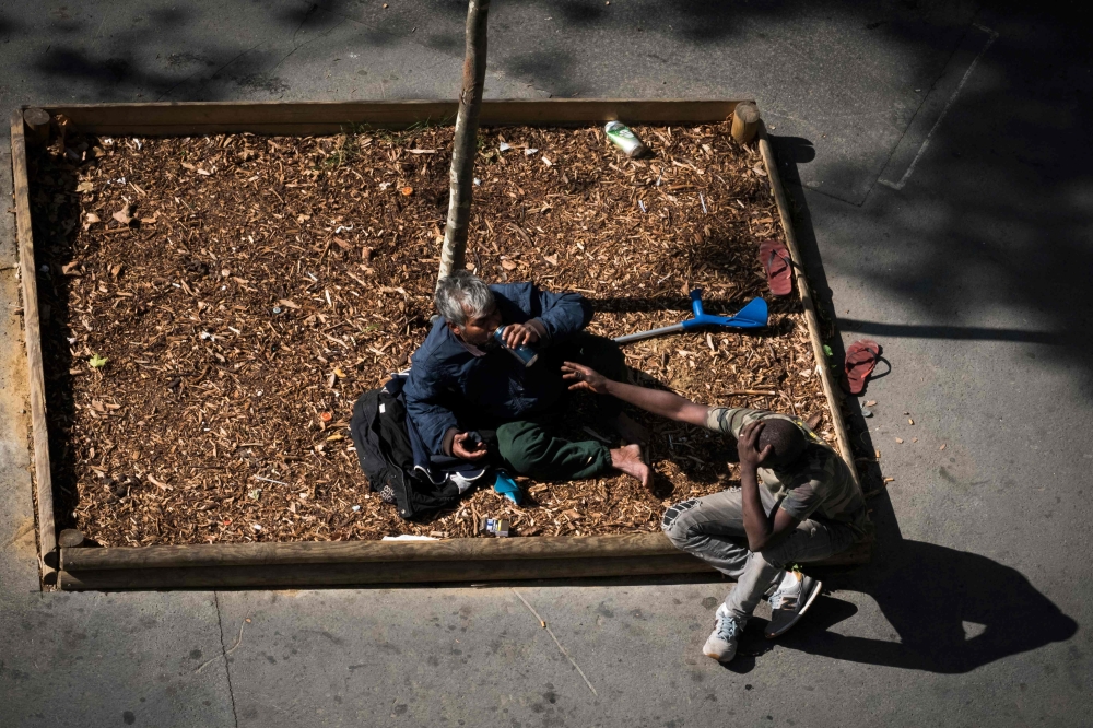 Two homeless men drink on the pavement in Paris on September 14, 2018. AFP/Joel Saget