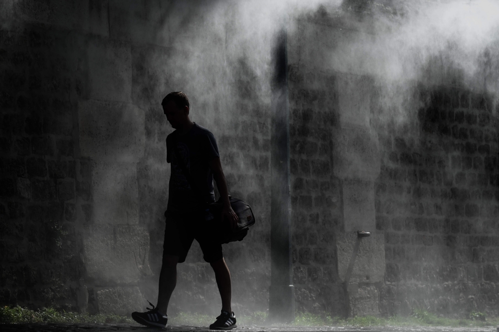 A man walks past a public water spray on the bank of the Seine river in Paris on July 25, 2019 as a new heatwave hits Europe. (AFP / Philippe LOPEZ)