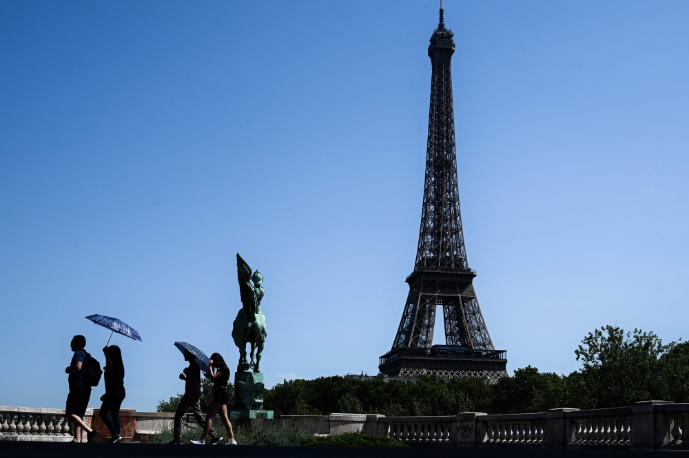 Tourist using umbrellas to protect themselves from a scorching sun walk on a bridge over the Seine river in front of the Eiffel Tower in Paris. (AFP / Philippe LOPEZ)