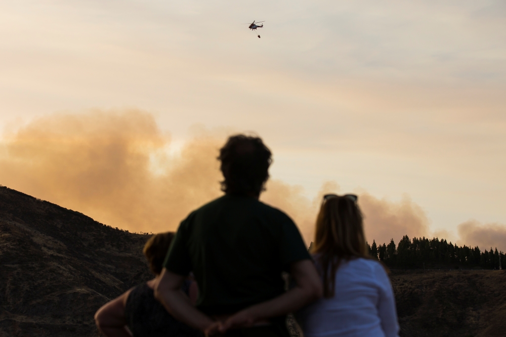 People who were evacuated from their homes look at a helicopter dropping water to fight a forest fire seen in the village of Valleseco, in the Canary Island of Gran Canaria, Spain, August 17, 2019. REUTERS/Borja Suarez
