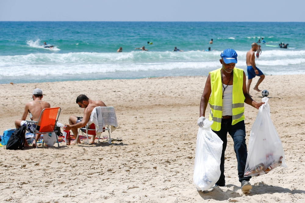 An employee of the Herzliya town hall collects plastics and other waste left behind by beachgoers, on one of the beaches of the Israeli coastal city on June 21, 2019.  AFP / Jack Guez 


 