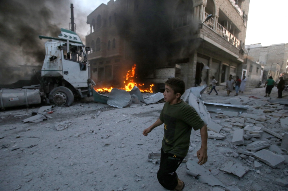 A young boy runs past a fire started in a building following a reported airstrike by Syrian regime forces in the town of Maaret al-Numan in Syria's northwestern Idlib province on August 28, 2019. / AFP / Abdulazez Ketaz
