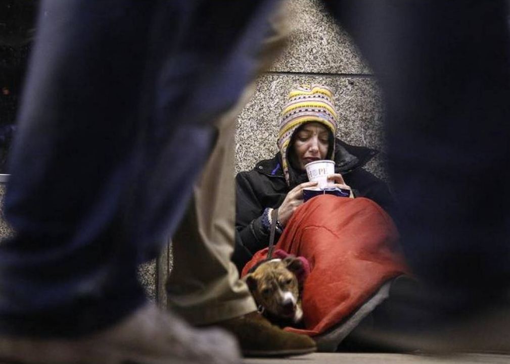 A homeless woman from north Wales sits huddled under a sleeping bag next to her dog in a shopping arcade near the Victoria rail station in London, December 14, 2012. Reuters/Chris Helgren