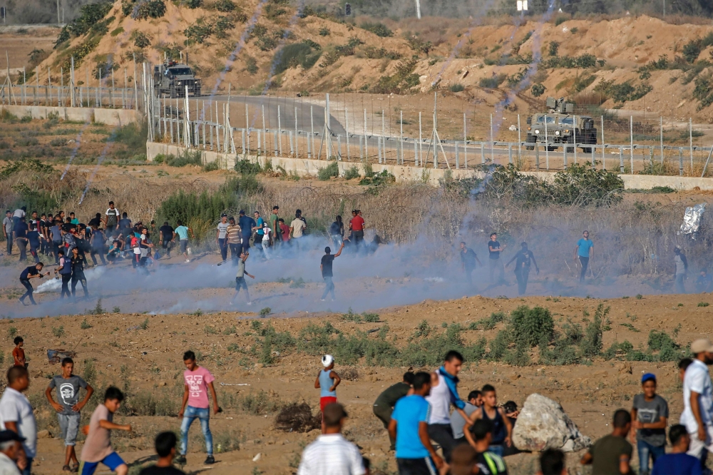 Palestinian protesters flee from tear gas fired by Israeli forces across the fence during clashes along the border with Israel near Bureij in the central Gaza Strip on August 30, 2019. AFP / Mohammed Abed 