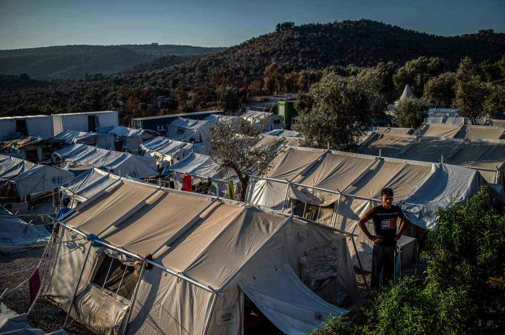 A migrant stands outside amid tents at the official refugee camp of Moria on the Greek island of Lesbos, on August 31, 2019.  AFP / ANGELOS TZORTZINIS