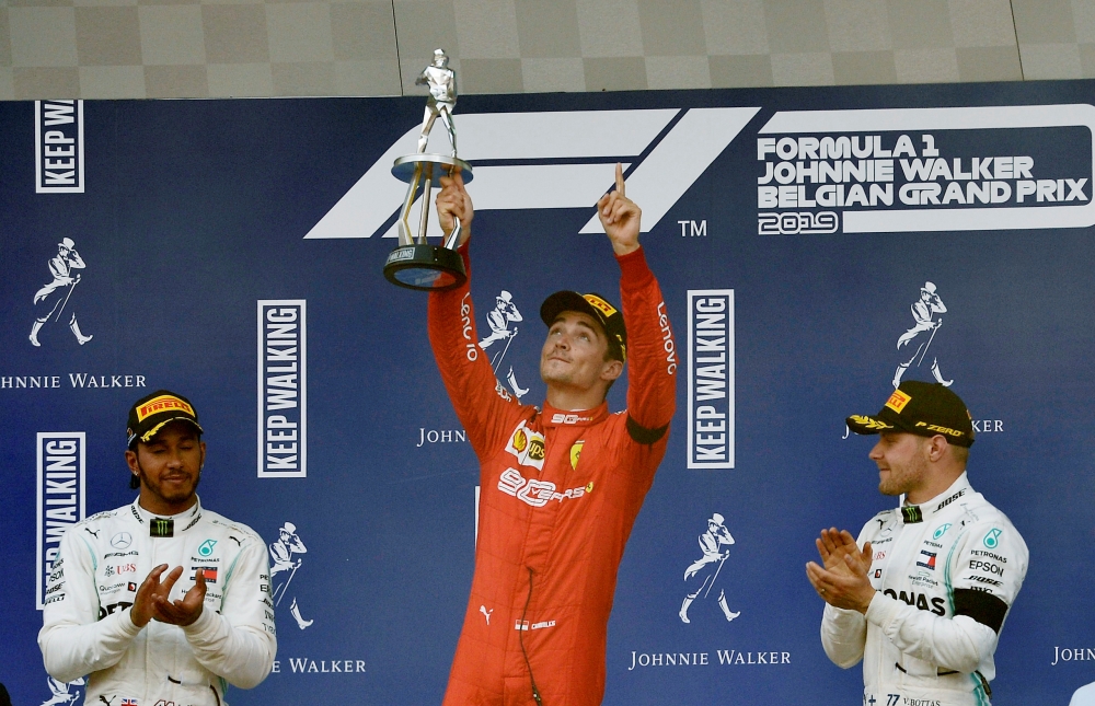 Ferrari's Charles Leclerc celebrates with a trophy on the podium after winning the race as he applauded by second placed Mercedes' Lewis Hamilton and third placed Mercedes' Valtteri Bottas REUTERS/Johanna Geron