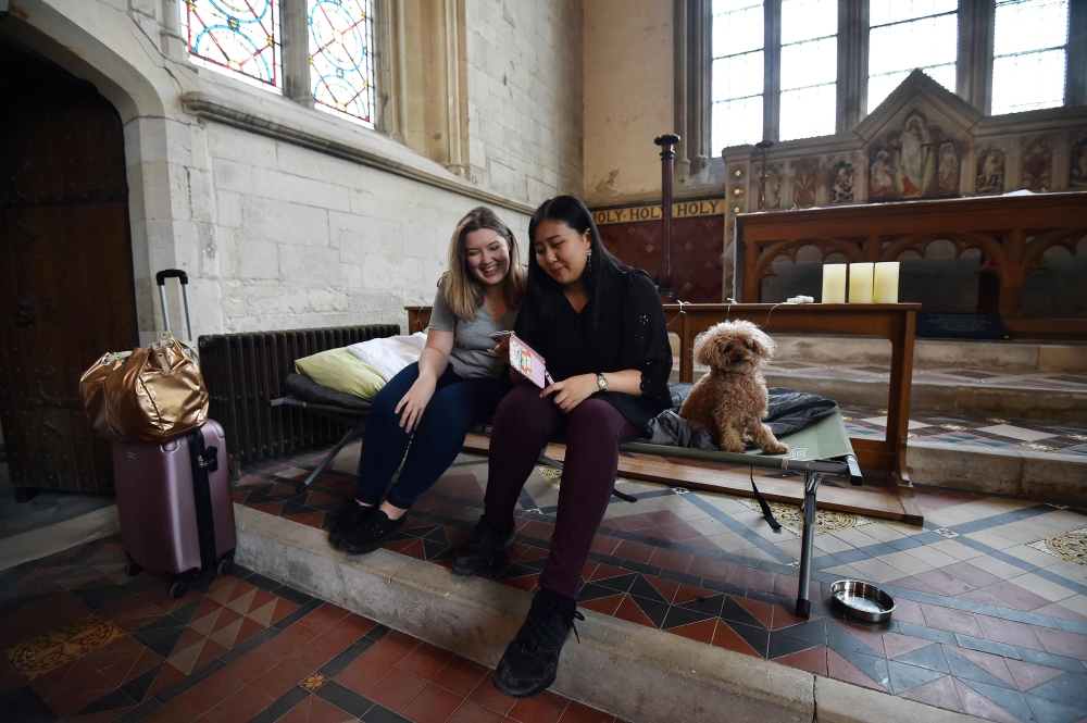 Andrea Stewart (L) and Kae Ono sit with Coco the dog as they settle in at St Mary's Church, where guests can pay to stay overnight in what is known as 'champing', in Edlesborough, Buckinghamshire on September 2, 2019.  AFP / Glyn Kirk 