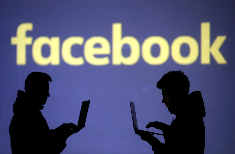 Silhouettes of laptop users are seen next to a screen projection of Facebook logo in this picture illustration dated  March 28, 2018. Reuters/Dado Ruvic