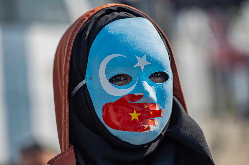 A demonstrator wears a mask painted with the colours of the flag of East Turkestan and a hand bearing the colours of the Chinese flag during a protest in front of the Chinese consulate in Istanbul on October 1, 2019. AFP / Yasin Akgul
 