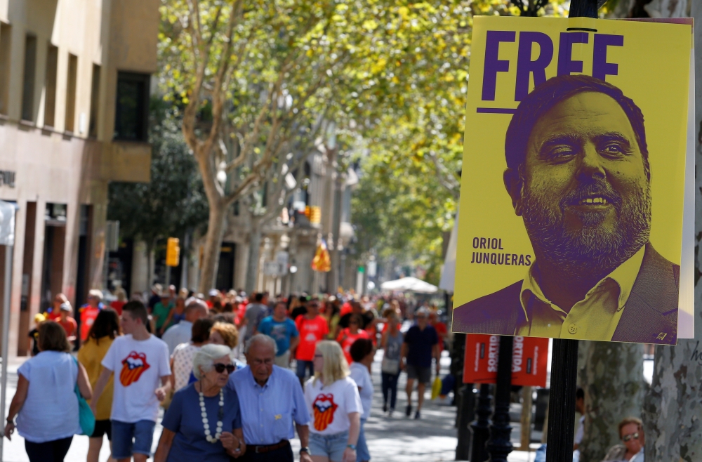 FILE PHOTO: People walk past a banner depicting dismissed Catalan Vice President Oriol Junqueras, currently in custody awaiting trial on charges of sedition, rebellion and misappropriation of public funds, during Catalonia's national day 'La Diada' in Bar