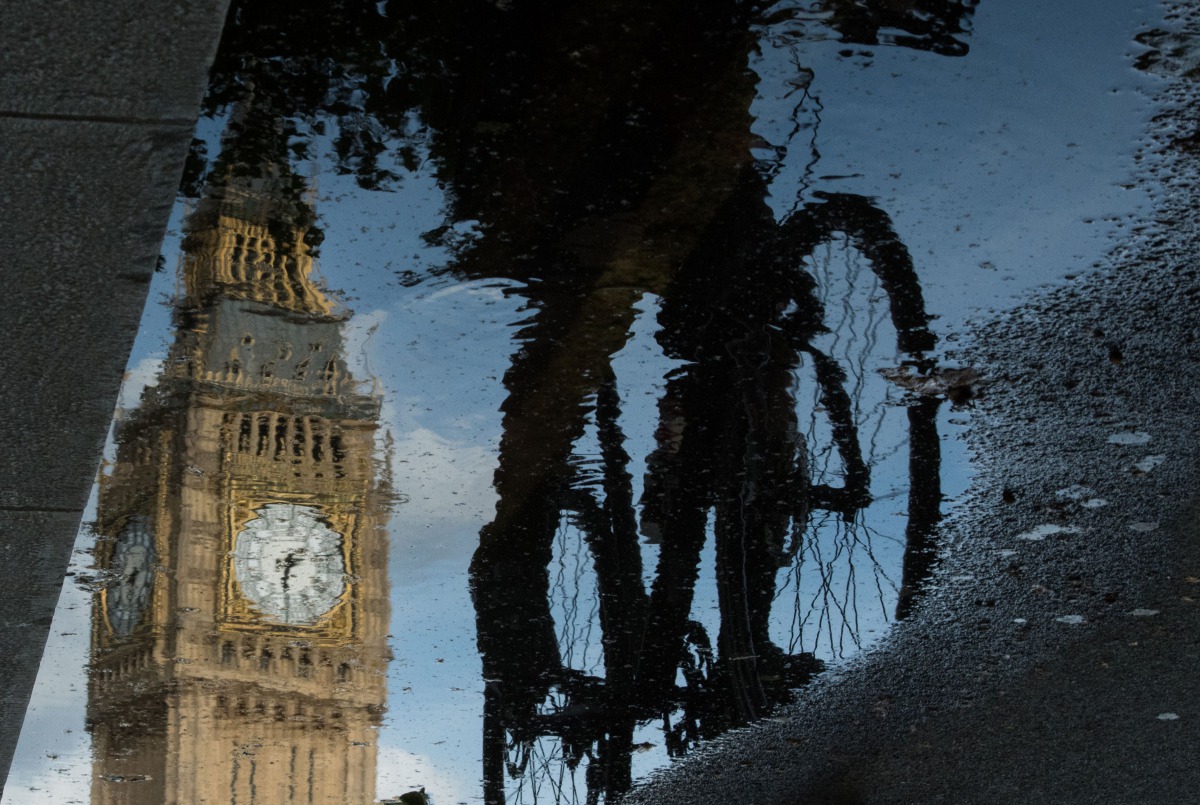 Big Ben is reflected in a puddle as a cyclist rides by in London on 27 June, 2016. AFP / Leon Neal