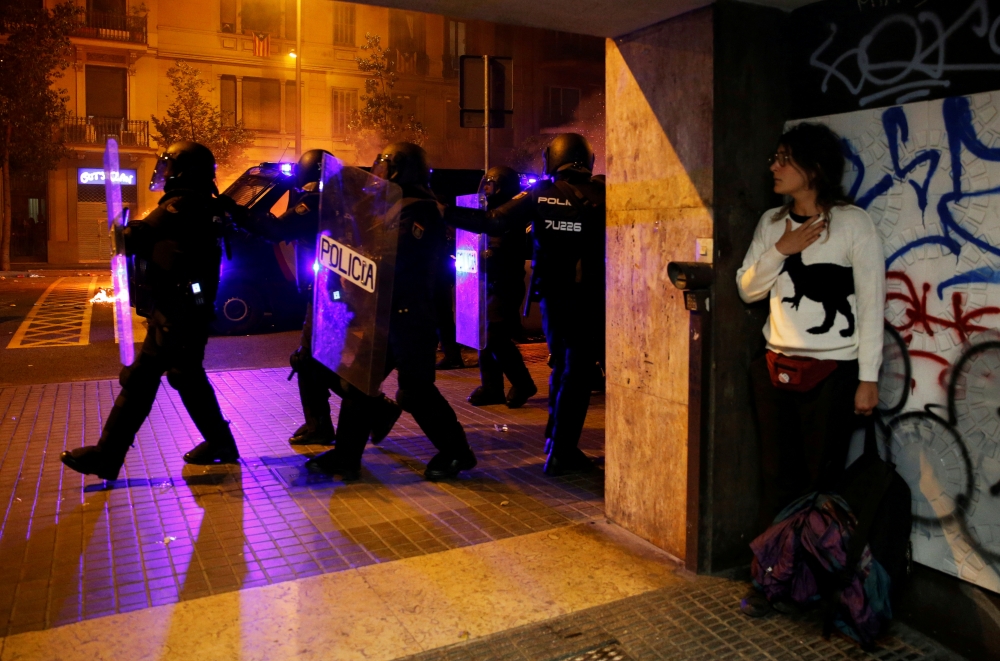 A woman takes cover as police officers walk past during a protest after a verdict in a trial over a banned Catalonia's independence referendum, in Barcelona, Spain, October 16, 2019. Reuters/ Rafael Marchante