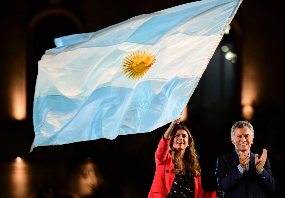 Argentina's President and presidential candidate of the Juntos por el Cambio party, Mauricio Macri (R), applauds as First Lady Juliana Awada was a national flag during the closing rally of his campaign in Cordoba, Argentina, on October 24, 2019. AFP / Ron