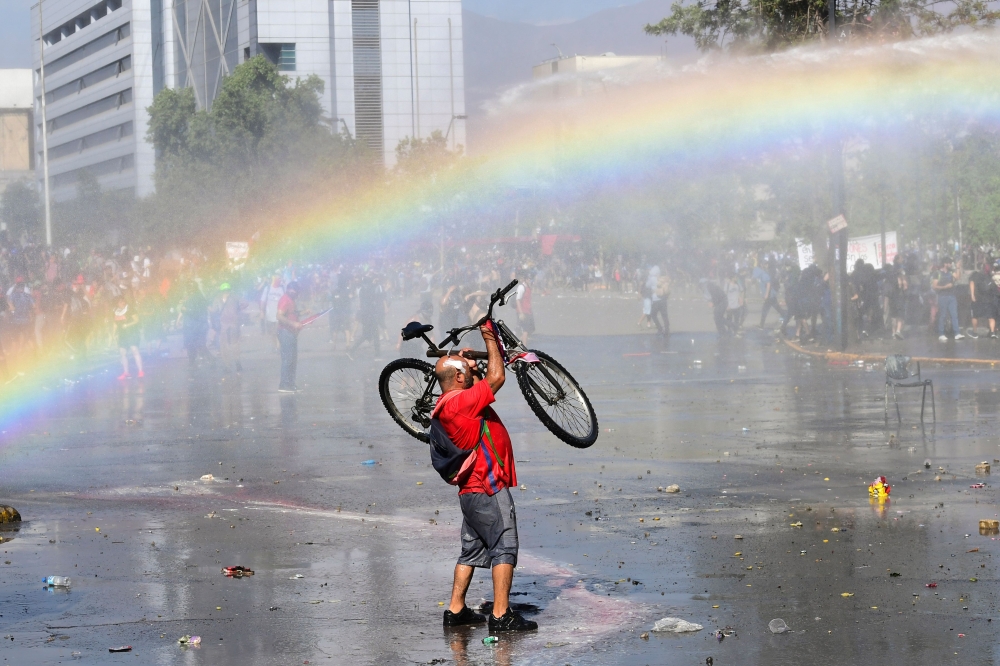 A demonstrator lifts his bike in the air during clashes with riot police in Santiago on October 24, 2019 after a week of street violence which erupted against a now suspended metro fare hike but spiralled into general discontent.  AFP / Martin Bernetti  