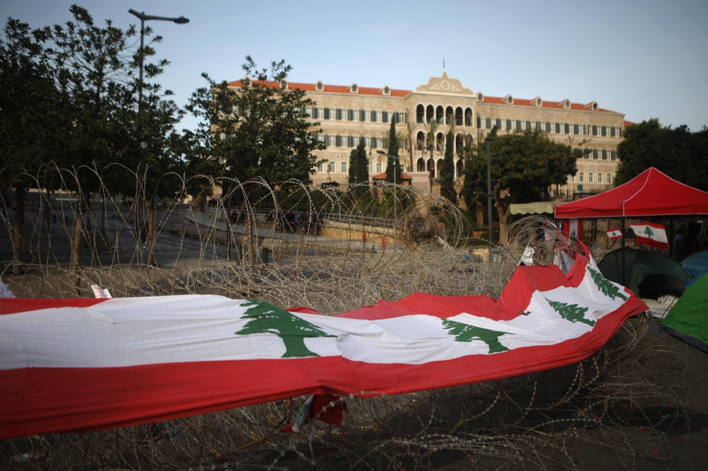 A long banner made up of Lebanese national flags hangs on barbed wire in front of the government headquarters, known as the Grand Serail, in the capital Beirut's downtown district on October 26, 2019.   AFP / Patrick BAZ