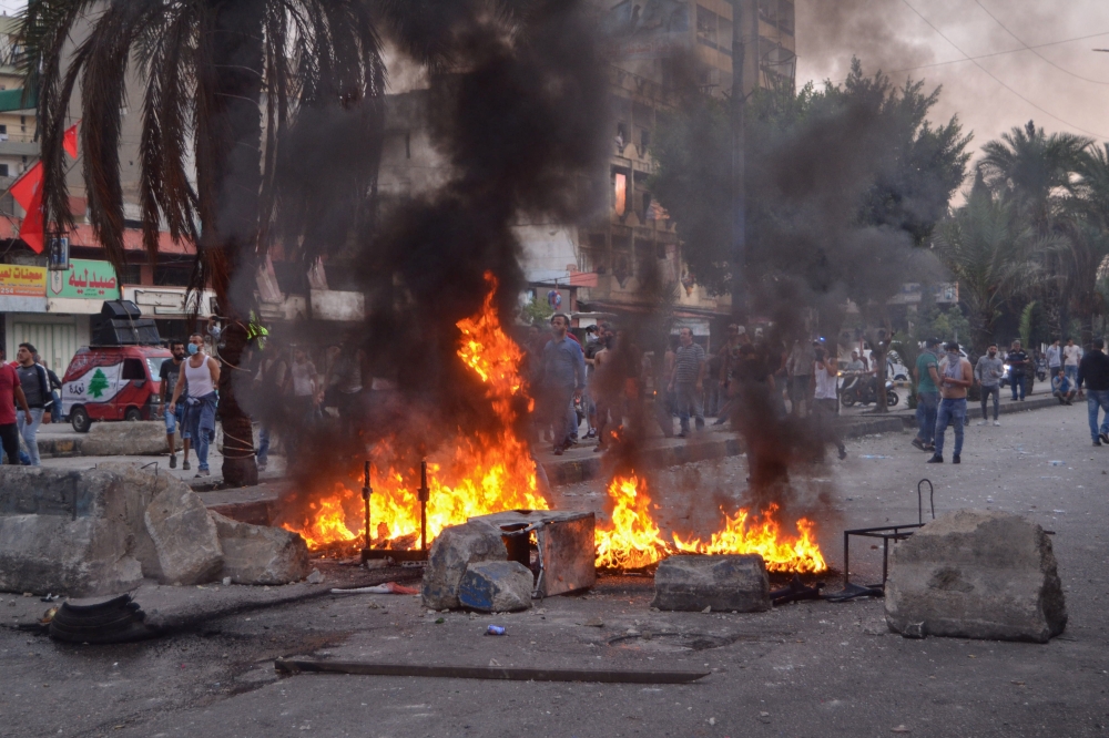 Lebanese anti-government protesters stand behind a burning barricade during a demonstration in Beddawi town on the outskirts of the northern Lebanese port city of Tripoli on October 26, 2019. (AFP / Fathi AL-MASSRI)