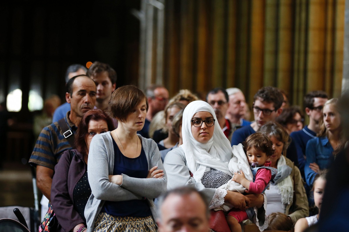 A Muslim woman carries a child as people attend a Mass in tribute to priest Jacques Hamel in the Rouen Cathedral on July 31, 2016. AFP