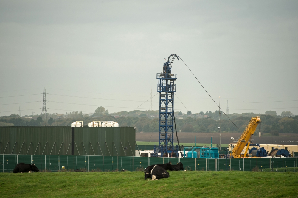(FILES) In this file photo taken on October 16, 2018 cows graze in a field as work gets under way at the Preston New Road drill site where energy firm Cuadrilla Resources have commenced fracking (hydraulic fracturing) operations to extract shale gas, near