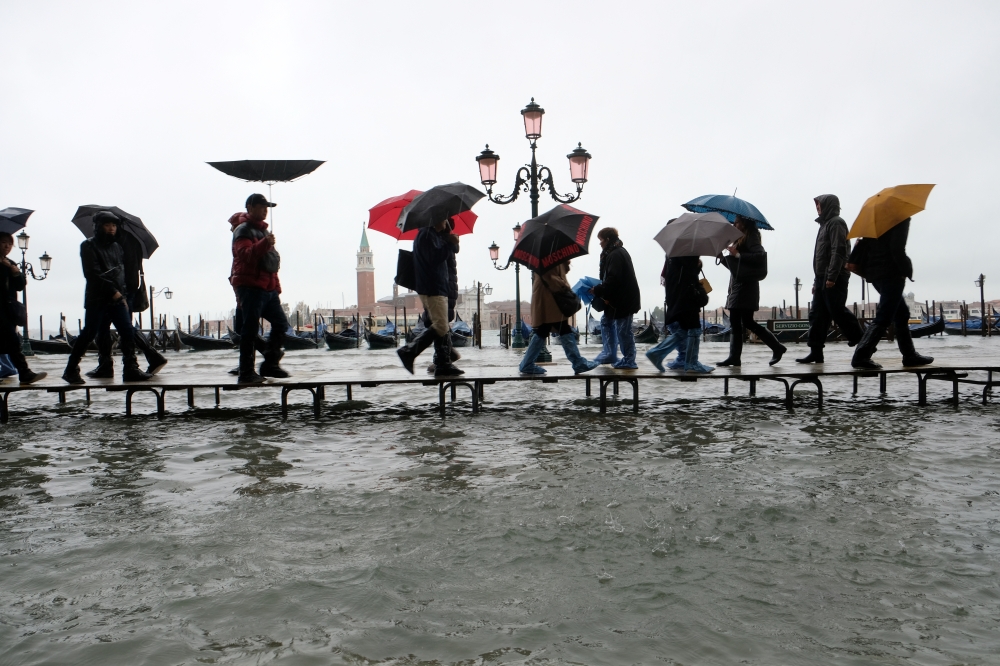 People walk on a catwalk in the flooded St.Mark's Square during a period of seasonal high water in Venice, Italy November 12, 2019. Reuters/Manuel Silvestri
 