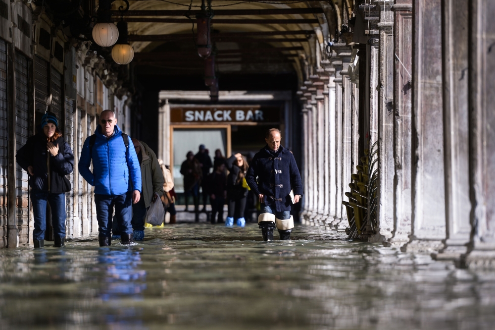 People walk across a floodedarcade by St. Mark's Square on November 14, 2019 in Venice. (AFP / Filippo MONTEFORTE)