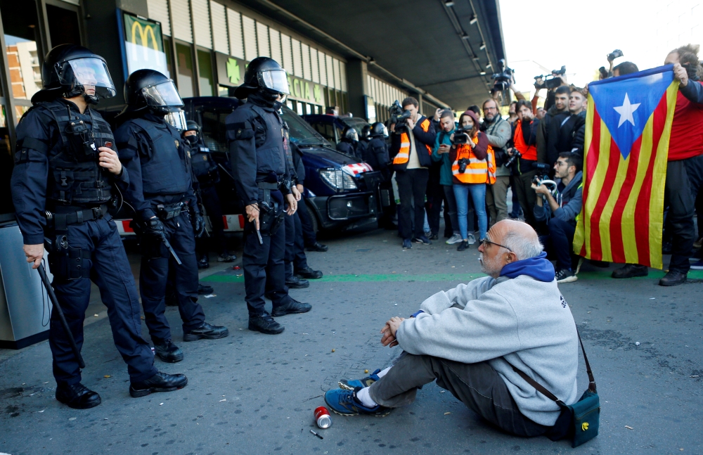 A man sits on the ground in front of riot police officers as Catalan separatist protesters attend a demonstration outside the Sants train station in Barcelona, Spain November 16, 2019. REUTERS/Enrique Calvo