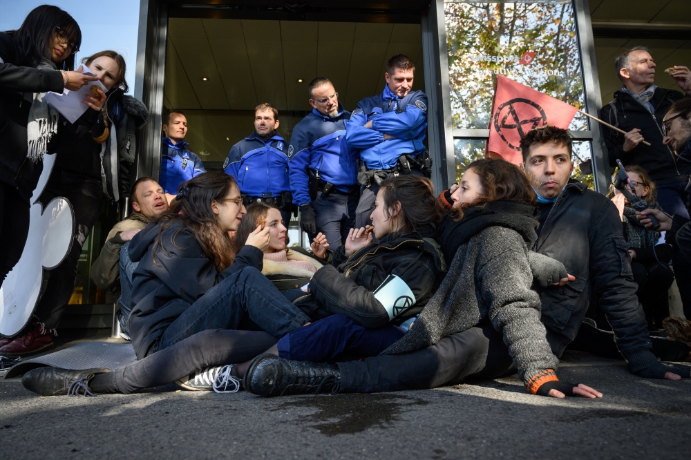 Activists seat in front of police officers to blocking an entrance at Geneva airport's private jet terminal, during a protest by the climate change action group Extinction Rebellion (XR), on November 16, 2019. / AFP / Fabrice Coffrini 