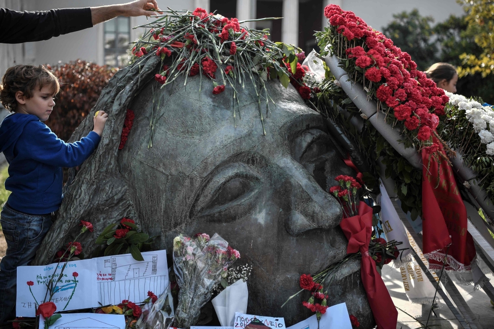 A woman places a red carnations on the monument in memory of the victims of the 1973 student's uprising against the US-backed military junta at the Athens' polytechnic school on November 16, 2019.  AFP / Louisa Gouliamaki 