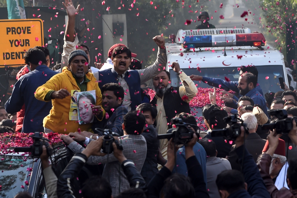 Supporters of Pakistan Muslim League Nawaz (PML-N) gather around a vehicle, covered with rose petals, carrying the ailing former Pakistani prime minister Nawaz Sharif as he travels to Lahore airport prior to his departure for abroad for medical treatment,
