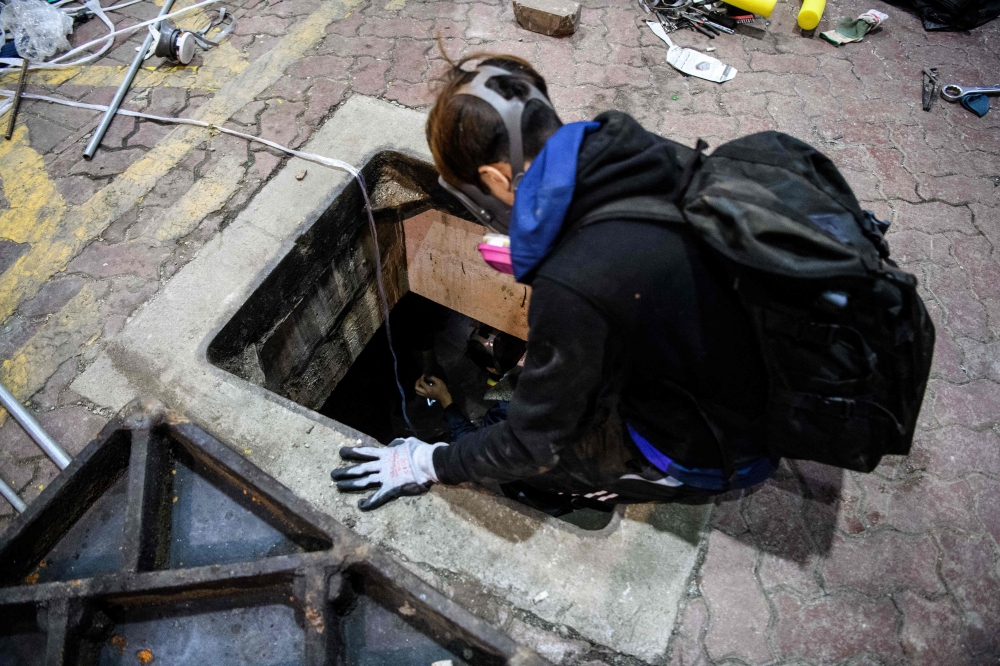 A protester climbs down into a sewer entrance as he and others try to find an escape route from the Hong Kong Polytechnic University in the Hung Hom district of Hong Kong, early morning on November 19, 2019. AFP / Anthony Wallace 