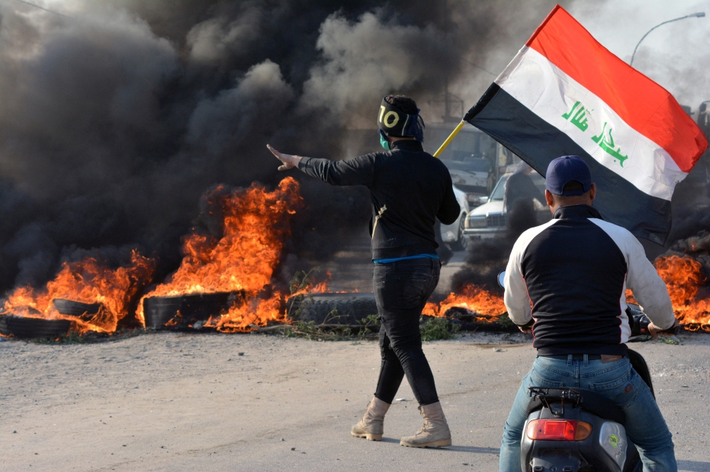 A demonstrator holds an Iraqi flag near burning tires during ongoing anti-government protests in Nassiriya, Iraq November 24, 2019. REUTERS/Ahmed Dhahi 