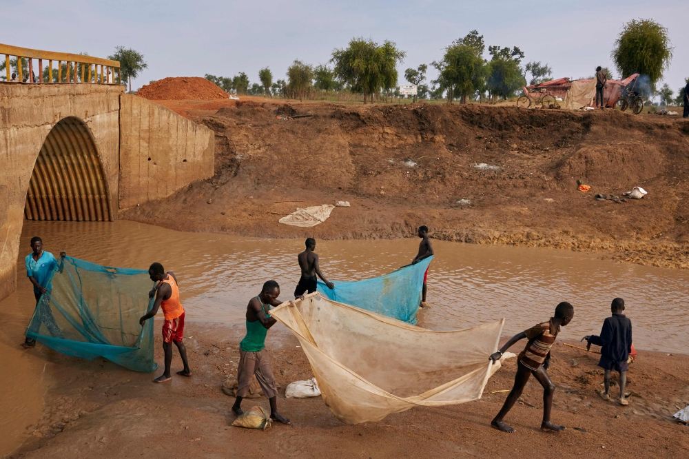 Residents of Yusuf Batir refugee camp fish together with the local host community at a stream formed as a result of intense flooding in Maban, South Sudan on November 26, 2019. AFP / Alex McBride
 
