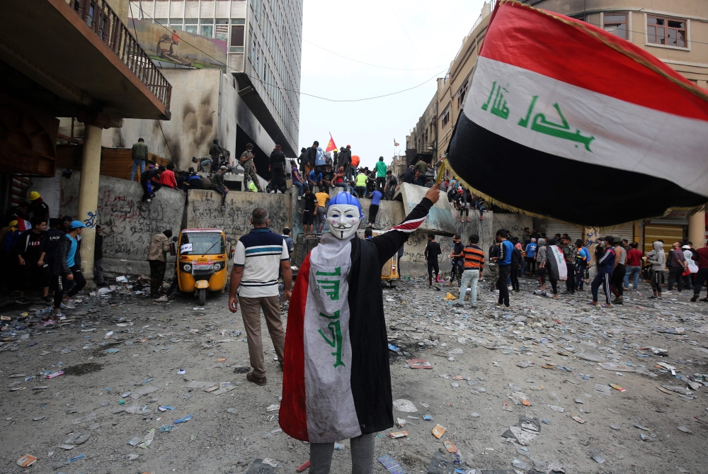 An Iraqi demonstrator wearing a Guy Fawkes mask in reverse and draped in a national flag waves another national flag before others celebrating the resignation of Prime Minister Adel Abdul-Mahdi's government, during a demonstration along Rasheed Street in 