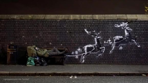 A man lays on a bench next to a new mural by Banksy in Birmingham, Britain, December 9, 2019, in this picture obtained from social media. @banksy/Instagram via Reuters 
