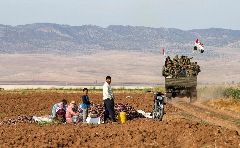 Syrian soldiers in a truck past people sitting in a field with harvested aubergines in the eastern countryside of the city of Qamishli in the northeastern Hasakah province on November 5, 2019. AFP / Delil Souleiman