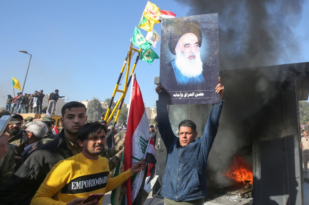 An Iraqi supporter lifts a picture of Iraq's top cleric Grand Ayatollah Ali Sistani during a rally in front of the US embassy in Baghdad, on December 31, 2019. (AFP / AHMAD AL-RUBAYE)