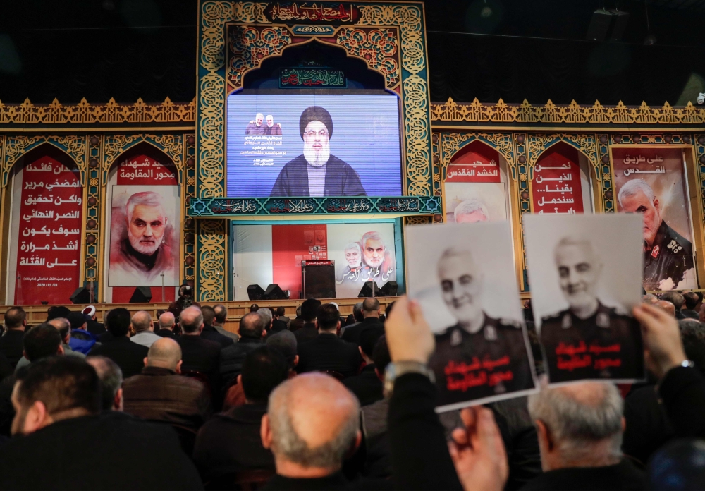 Supporters of Shiite Hezbollah movement hold posters of slain Iranian Major General Qasem Soleimani as the movement's leader Hasan Nasrallah delivers a speech on a screen, in the Lebanese capital Beirut's southern suburbs on January 5, 2020.  AFP / ANWAR 