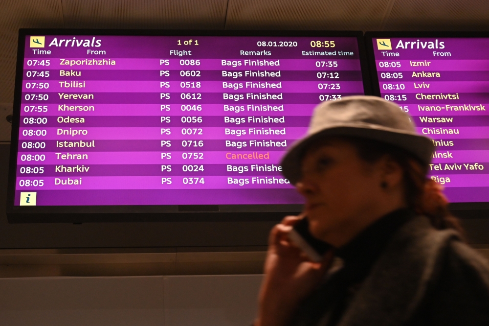 A woman uses a smartphone as she walks past an arrivals board displaying the Ukraine International Airlines Flight PS752 from Tehran marked as canceled at the Boryspil airport outside Kiev on January 8, 2020. AFP / Sergei Supinsky