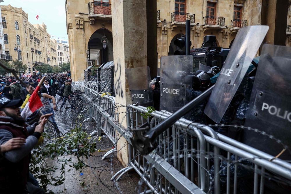 Lebanese security forces take cover behind riot shields during clashes with anti-government protesters in the central downtown district of the Lebanese capital near the parliament headquarters on January 18, 2020. / AFP / Anwar AMRO