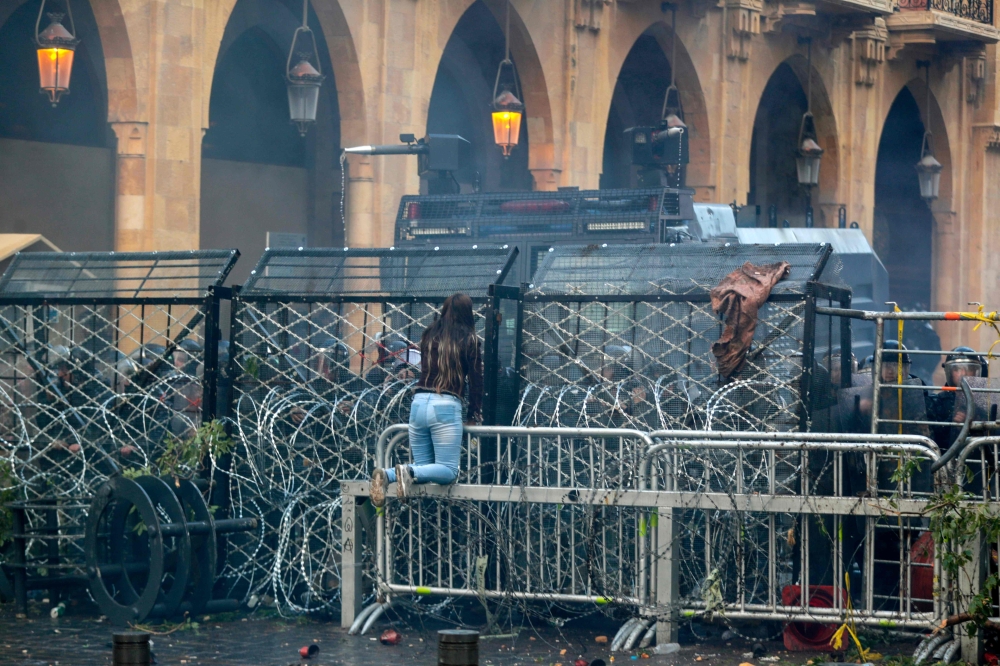 An anti-government protester climbs the police barricades during clashes with security forces in the central downtown district of the Lebanese capital Beirut near the parliament headquarters on January 18, 2020. / AFP / ANWAR AMRO