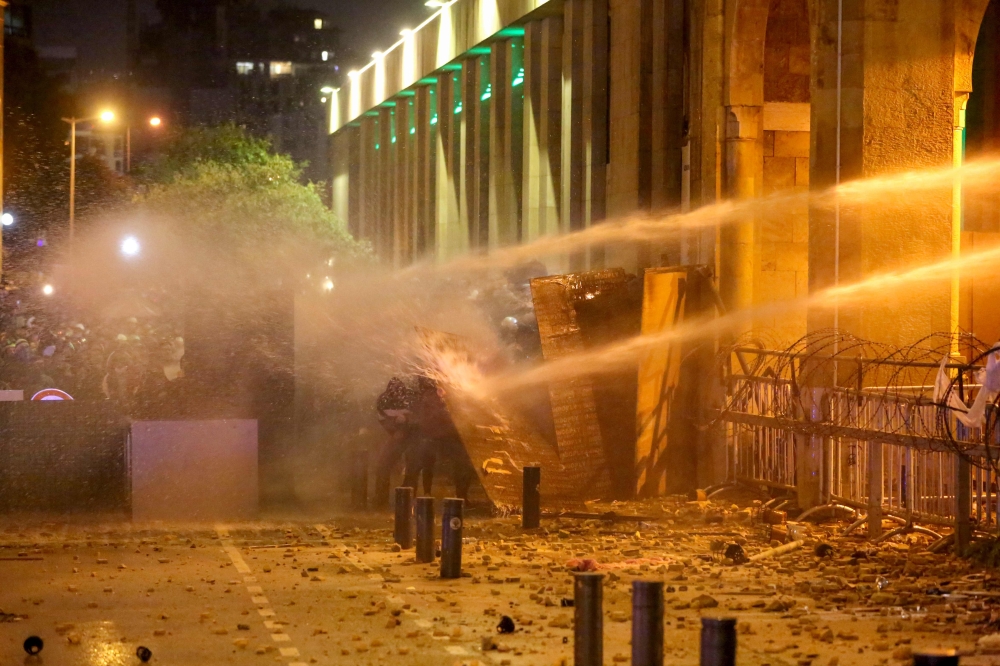 Lebanese protesters take cover as riot police spray them with water from behind a barricaded road leading to parliament in central Beirut  amid ongoing anti-government demonstrations. Lebanese anti-riot police fired rubber bullets and water cannons at sto
