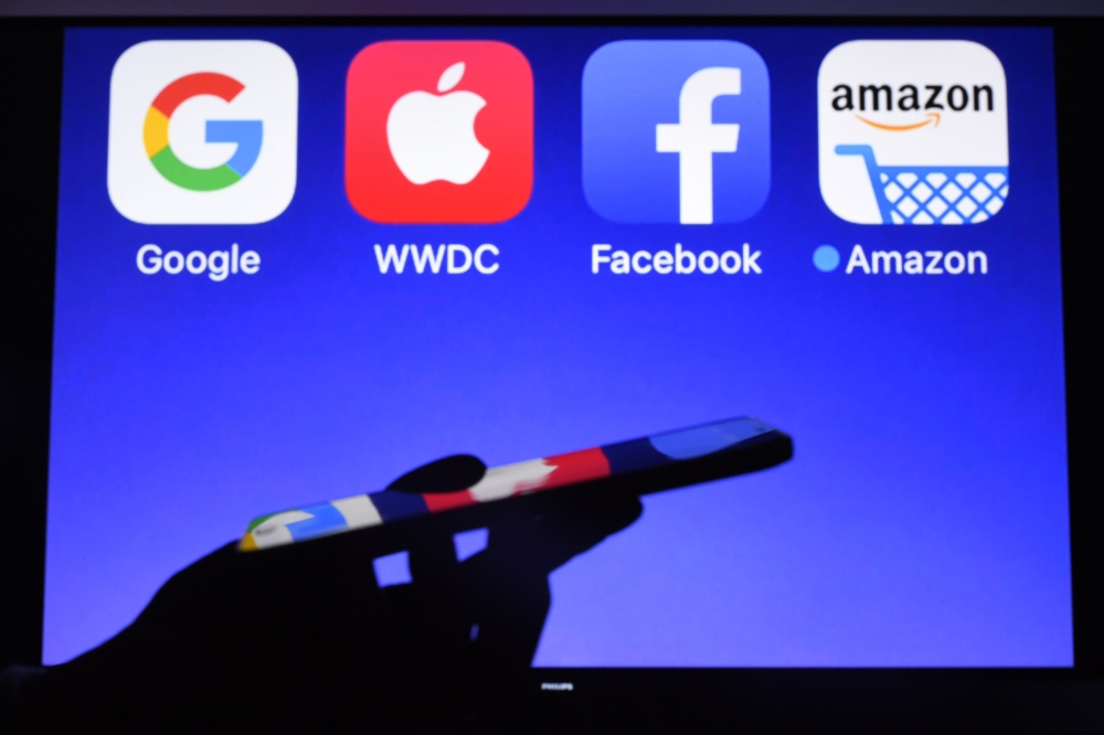 A smartphone being operated in front of GAFA (acronym for Google, Apple, Facebook and Amazon) logos as background in Hédé-Bazouges, western France on September 28, 2017. AFP / Damien Meyer. 