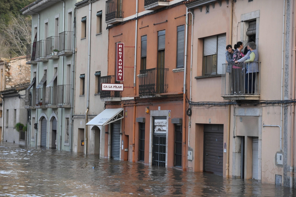 People looks at a flooded street from a balcony in Sarria de Ter on January 23, 2020, as storm Gloria batters Spanish eastern coast. AFP / Josep Lago
 
