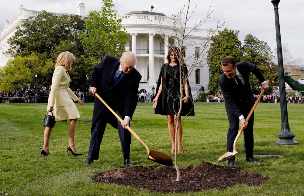 Donald Trump and Emmanuel Macron shovel dirt onto a freshly planted oak tree as first lady Melania Trump and Brigitte Macron watch on the South Lawn of the White House, April 23, 2018. Reuters /  Joshua Roberts