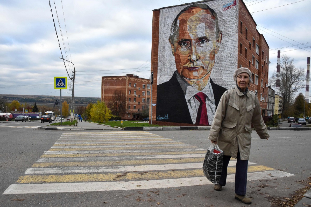 An elderly woman crosses a road in front a mural painting depicting Russian President Vladimir Putin in the town of Kashira, some 115 km southeast of Moscow on October 16, 2017. AFP / Vasily Maximov